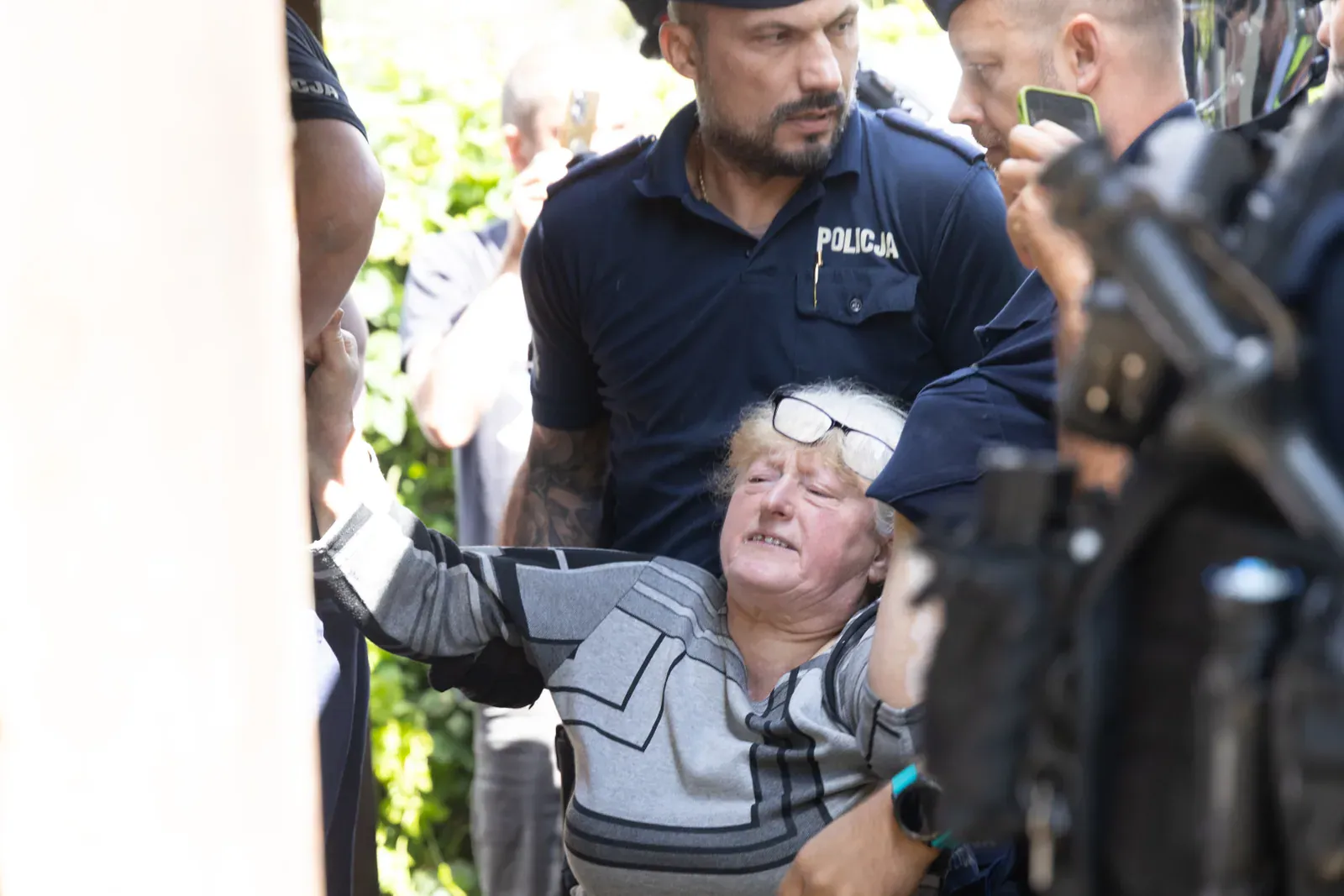 Policjanci wynoszą Bronisławę Waszkiewicz z ogrodu posesji