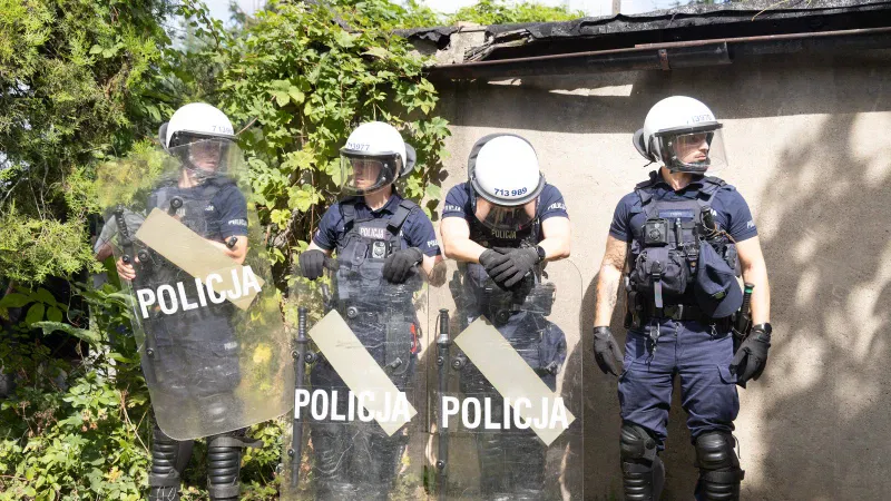 Kordon policjantów z tarczami na wąskiej alejce między ogrodami na osiedlu Maltańskim w Poznaniu