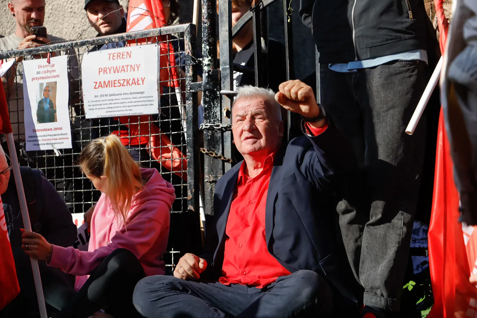 Piotr Ikonowicz siedzi przed bramą posesji, obok plakat „Teren prywatny zamieszkały” (9.36)