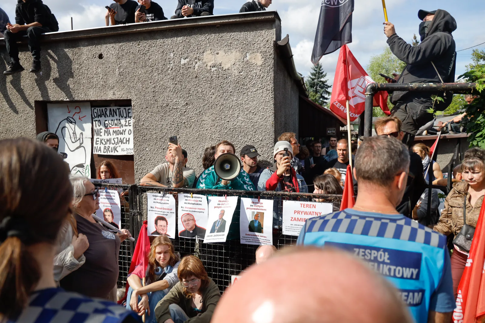 Megafon i blokada przed bramą, na dachu protestujący (10.50)