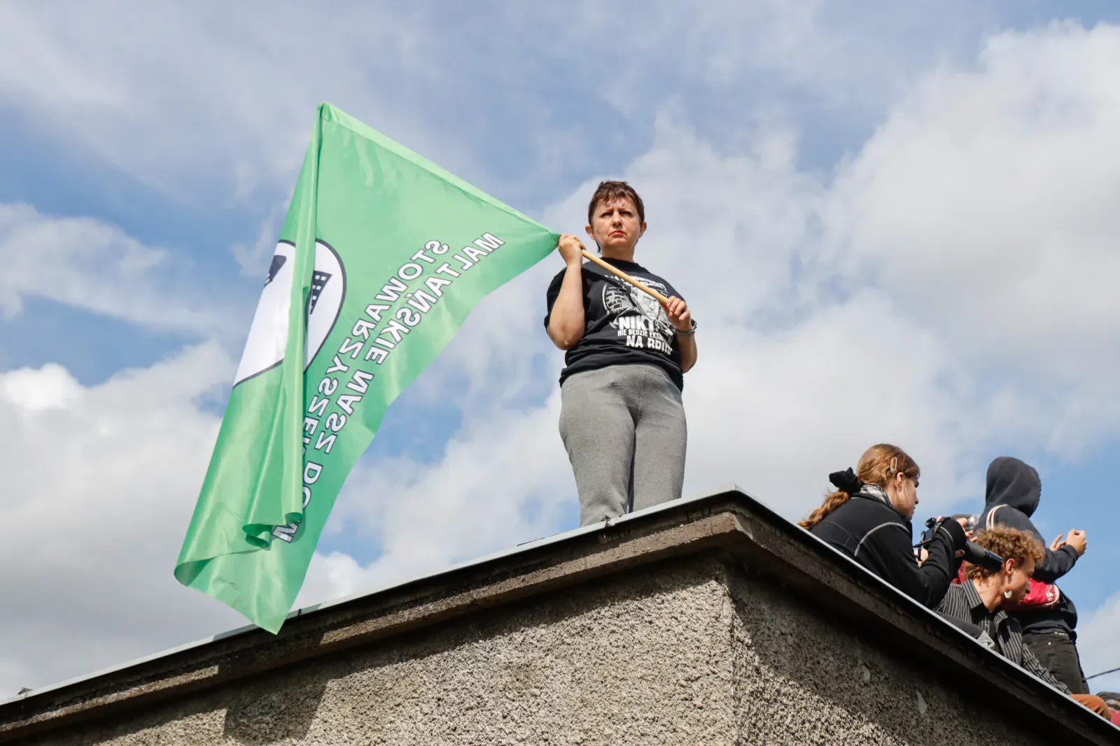 Kobieta na dachu domu macha zieloną flagą stowarzyszenia Maltańskie Nasz Dom