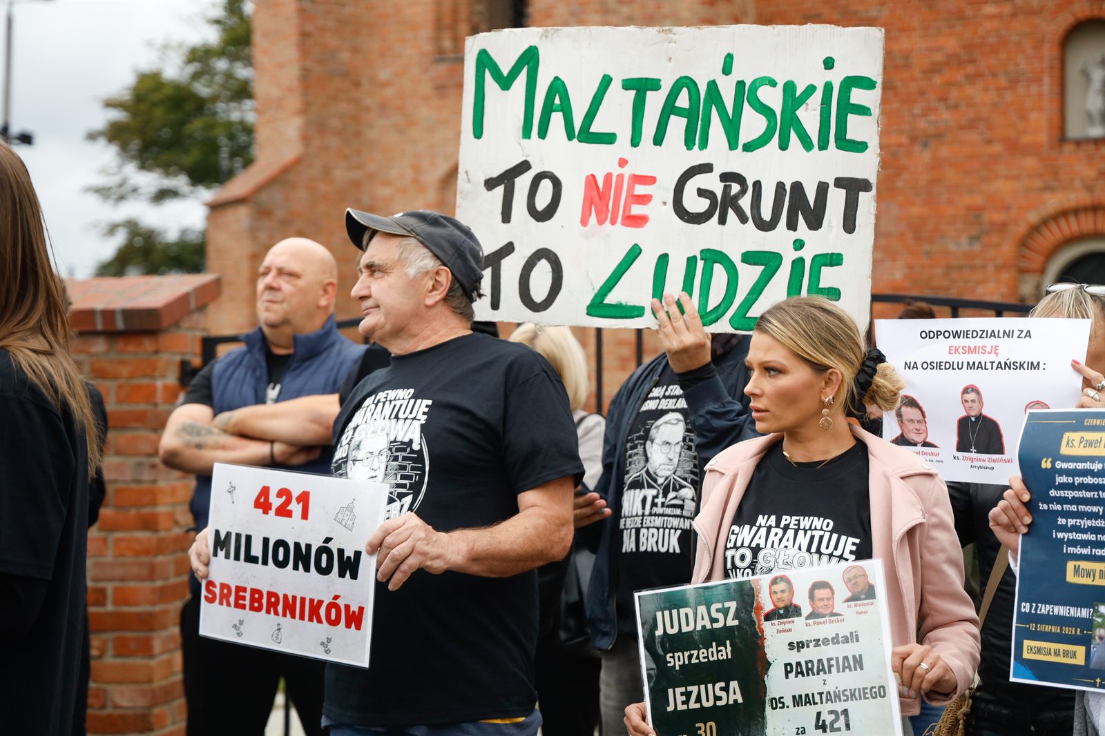 Kobieta unosi dużą tablicę z napisem „Maltańskie to nie grunt, to ludzie”, obok mężczyzna z kartką „421 milionów srebrników”
