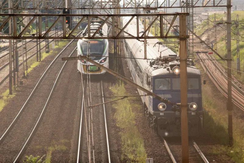 Pociąg PKP Intercity prowadzony lokomotywą i zielono-biały skład osobowy na sąsiednich torach wielotorowego szlaku kolejowego