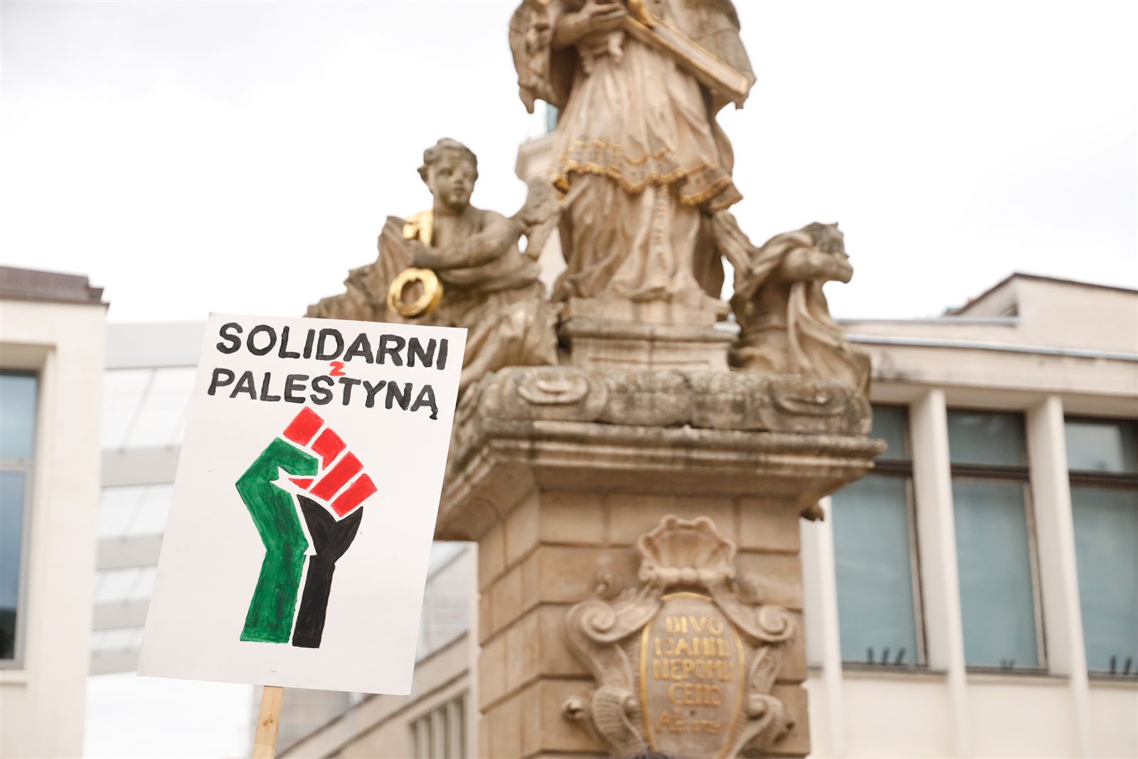Plakat „Solidarni z Palestyną” pod barokową figurą na Starym Rynku