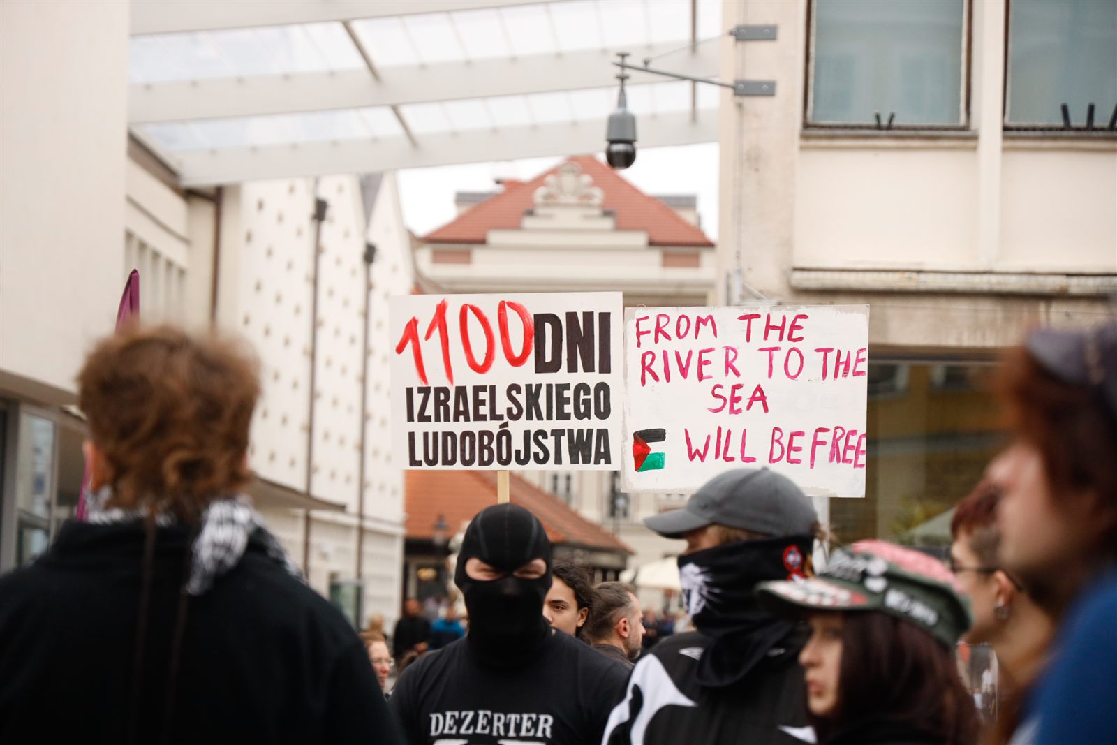 Dwie ręcznie malowane plansze nad głowami uczestników: „1100 dni izraelskiego ludobójstwa” i „From the river to the sea, Palestine will be free”