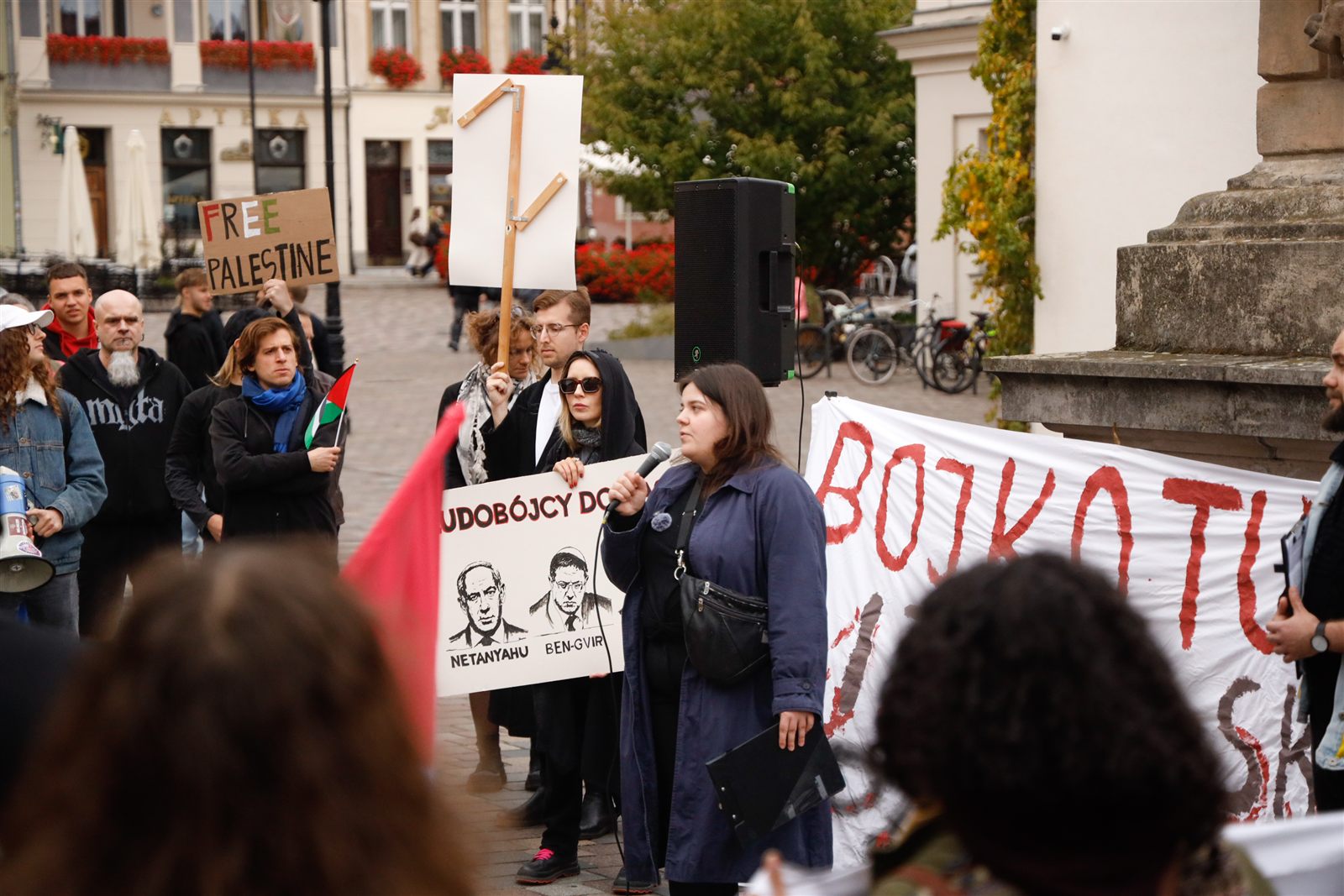 Mówczyni przed transparentem „Bojkotuj izraelski apartheid”