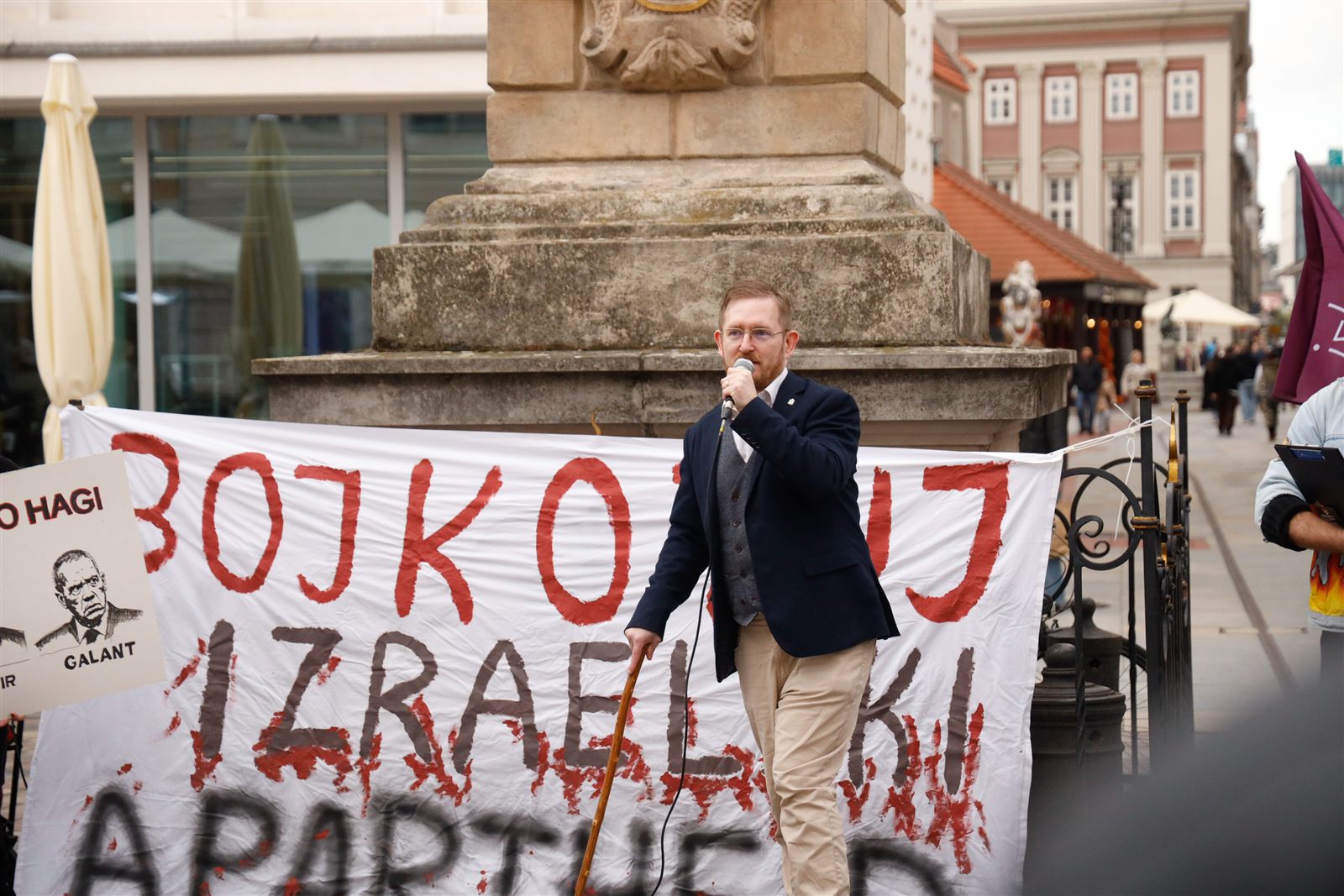 Łukasz Garczewski z mikrofonem przed transparentem z napisem „Bojkotuj izraelski apartheid”