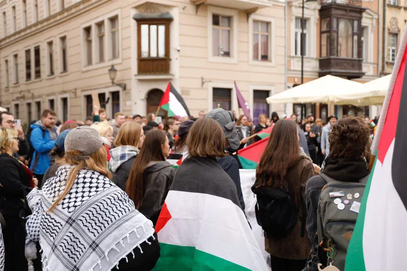 Uczestnicy demonstracji owinięci flagami Palestyny i w arafatkach stoją tyłem do obiektywu wśród tłumu na poznańskim Starym Rynku