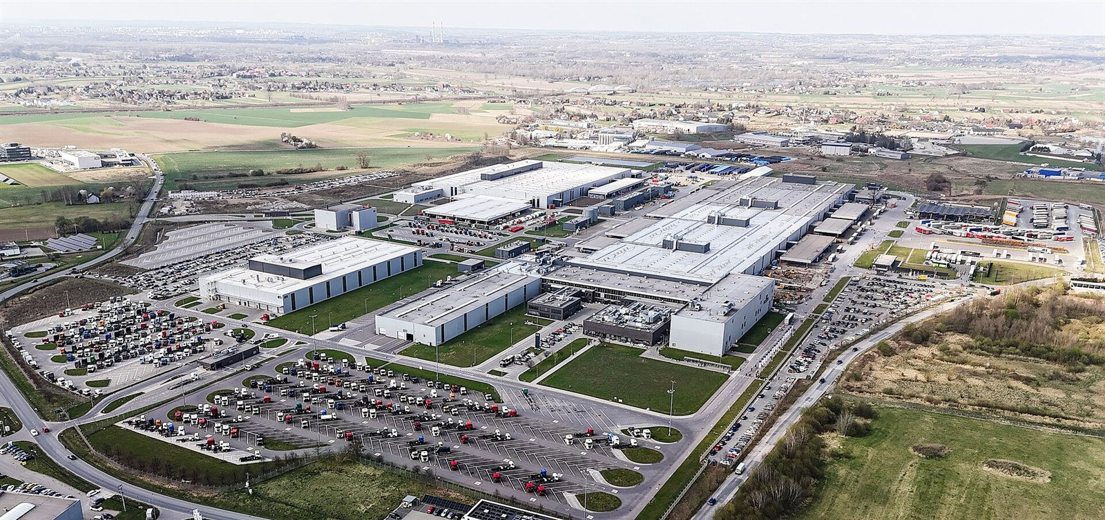 Fabryka ciężarówek MAN w Niepołomicach z lotu ptaka: hale produkcyjne, parkingi pełne ciągników siodłowych i pola dookoła
