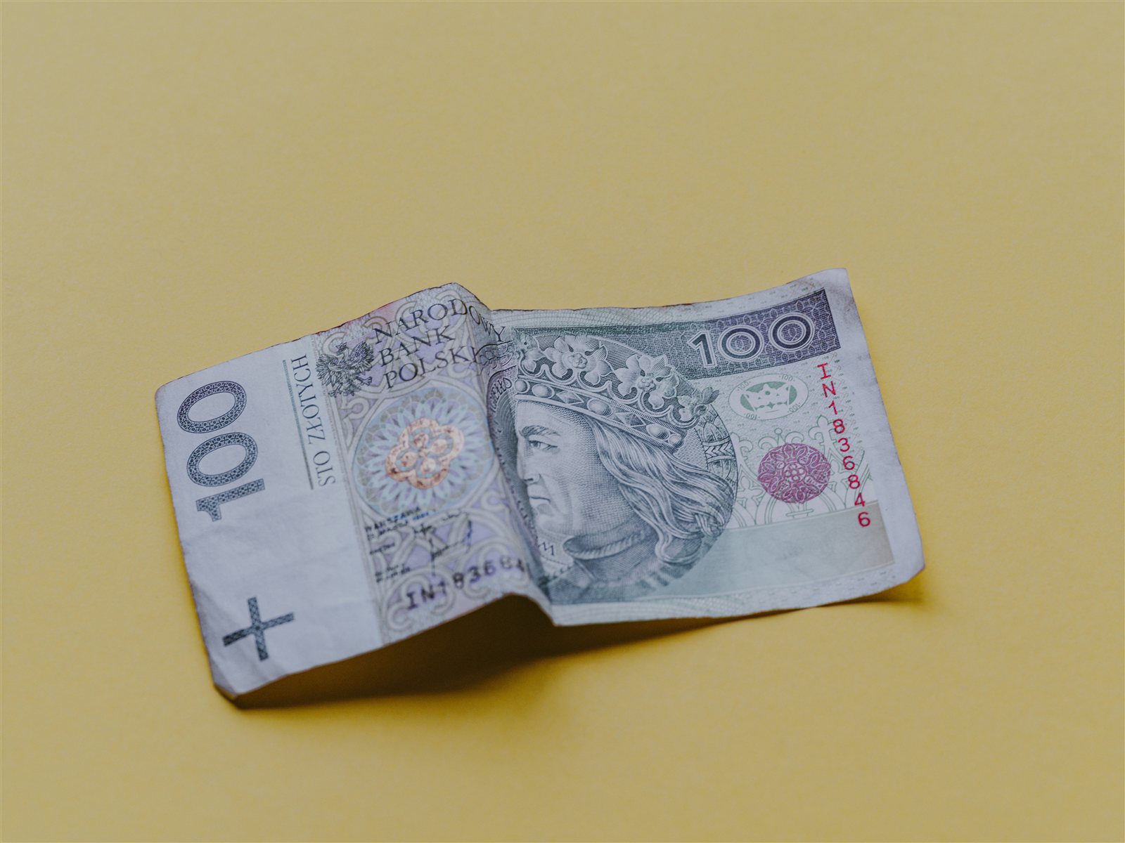 Pognieciony banknot 100 zł na żółtym tle