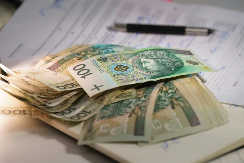 Plik banknotów stuzłotowych leży na wypełnionych formularzach obok długopisu